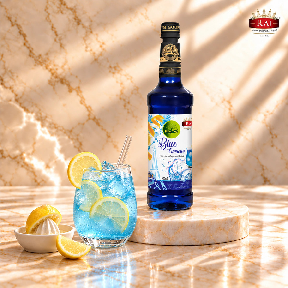 RAJ Pulpy Tree Blue Curacao syrup bottle beside a blue lagoon mocktail with ice, lemon and orange peel.