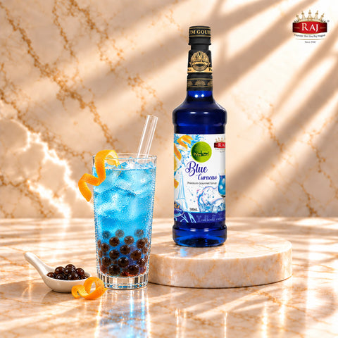 RAJ Pulpy Tree Blue Curacao syrup bottle beside blue bubble tea with tapioca pearls, ice and a wide straw.