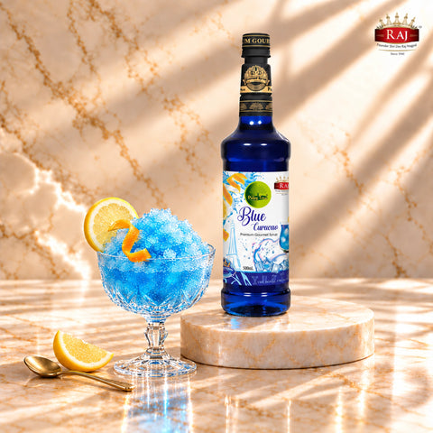 RAJ Pulpy Tree Blue Curacao syrup bottle beside a frozen blue citrus slush garnished with lemon and orange peel.