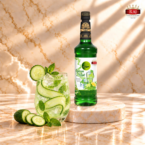 RAJ Pulpy Tree Green Mint syrup bottle beside a cucumber mint cooler with cucumber ribbons, fresh mint and ice.